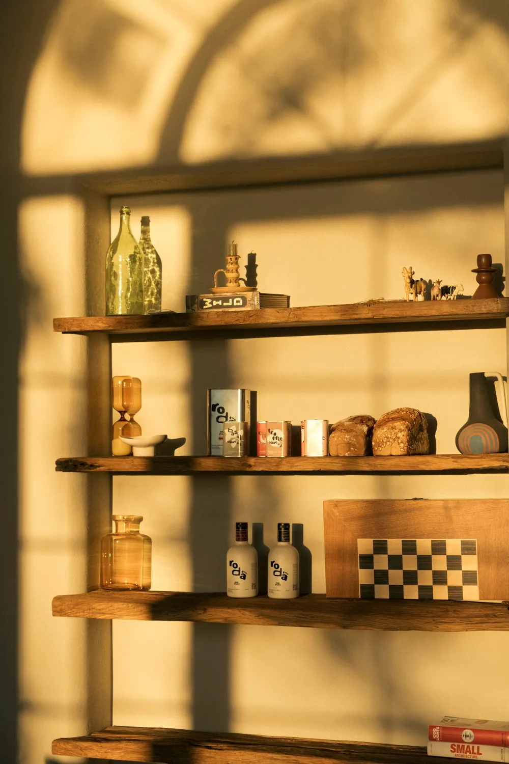 Warm sunlight across wall-mounted timber shelves with books and glass vases