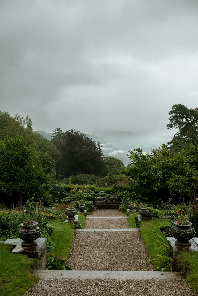 Gravel steps between stone urns leading to a misty valley view