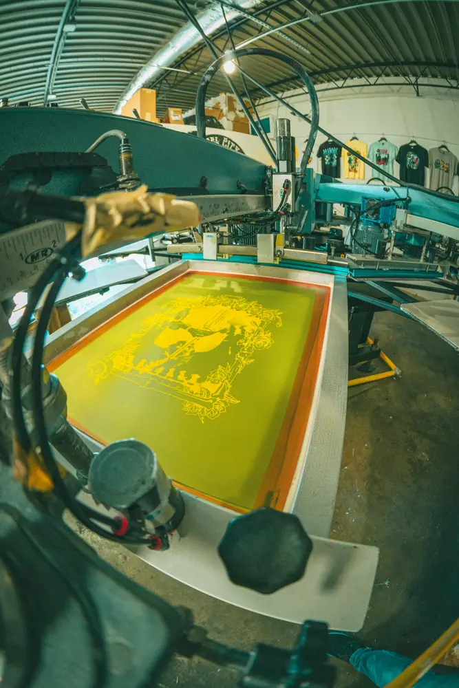 Screen-printing press with a bright yellow screen loaded on the platen