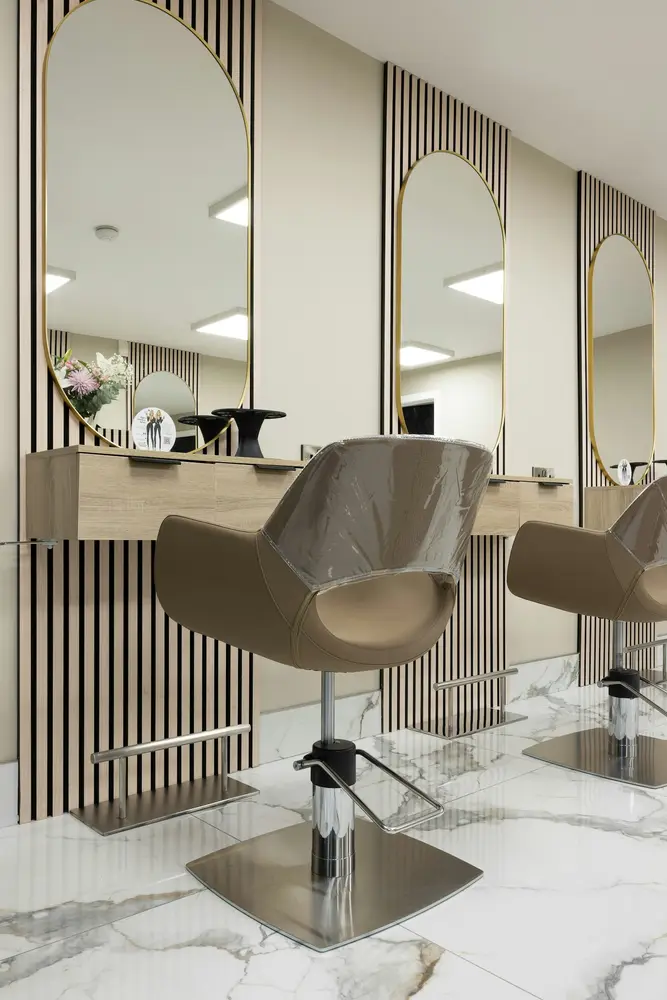 Detail of a salon station: arched mirror, oak shelf and a leather chair on marble floor